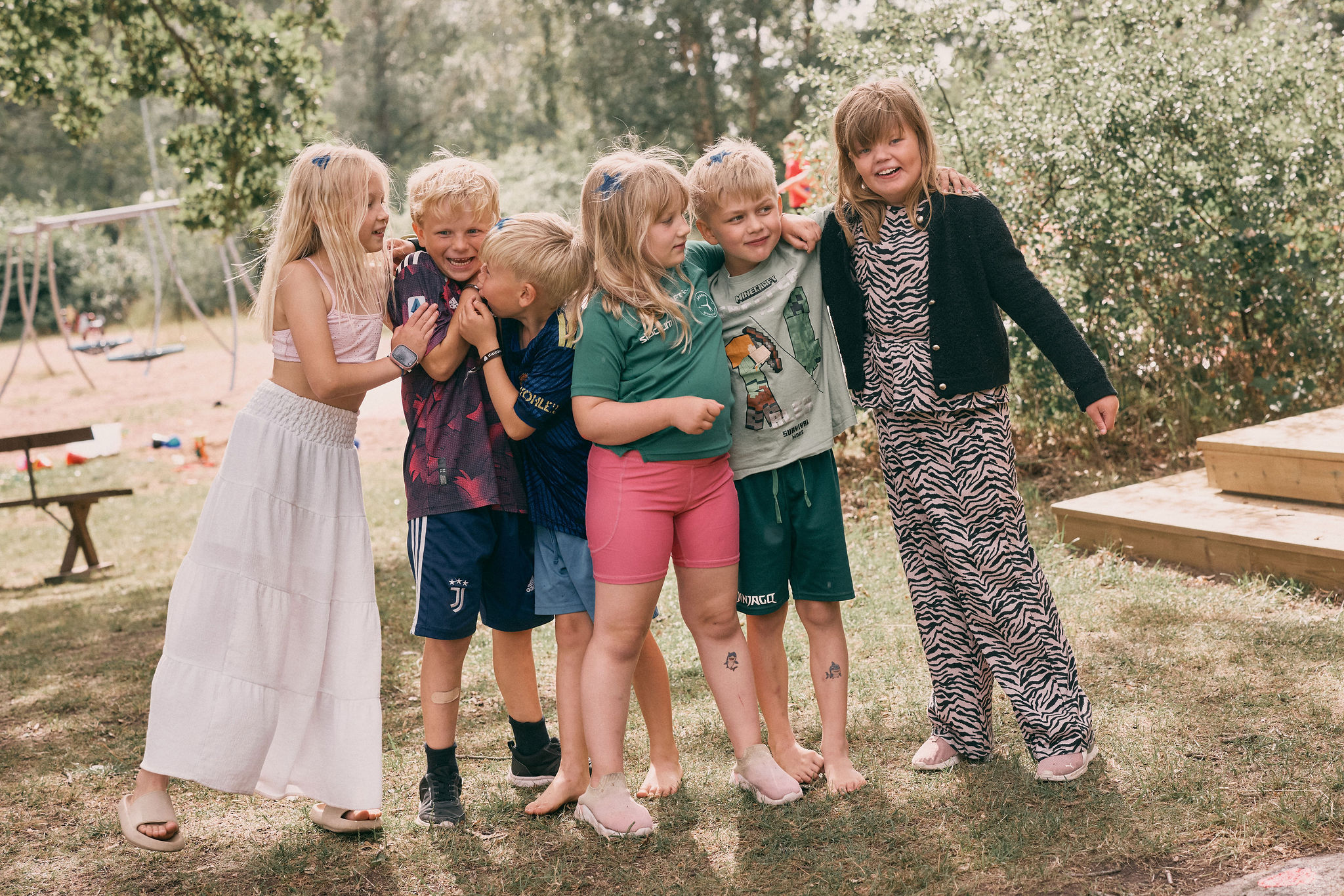 Sex barn står tätt tillsammans med armarna om varandra och skrattar.
