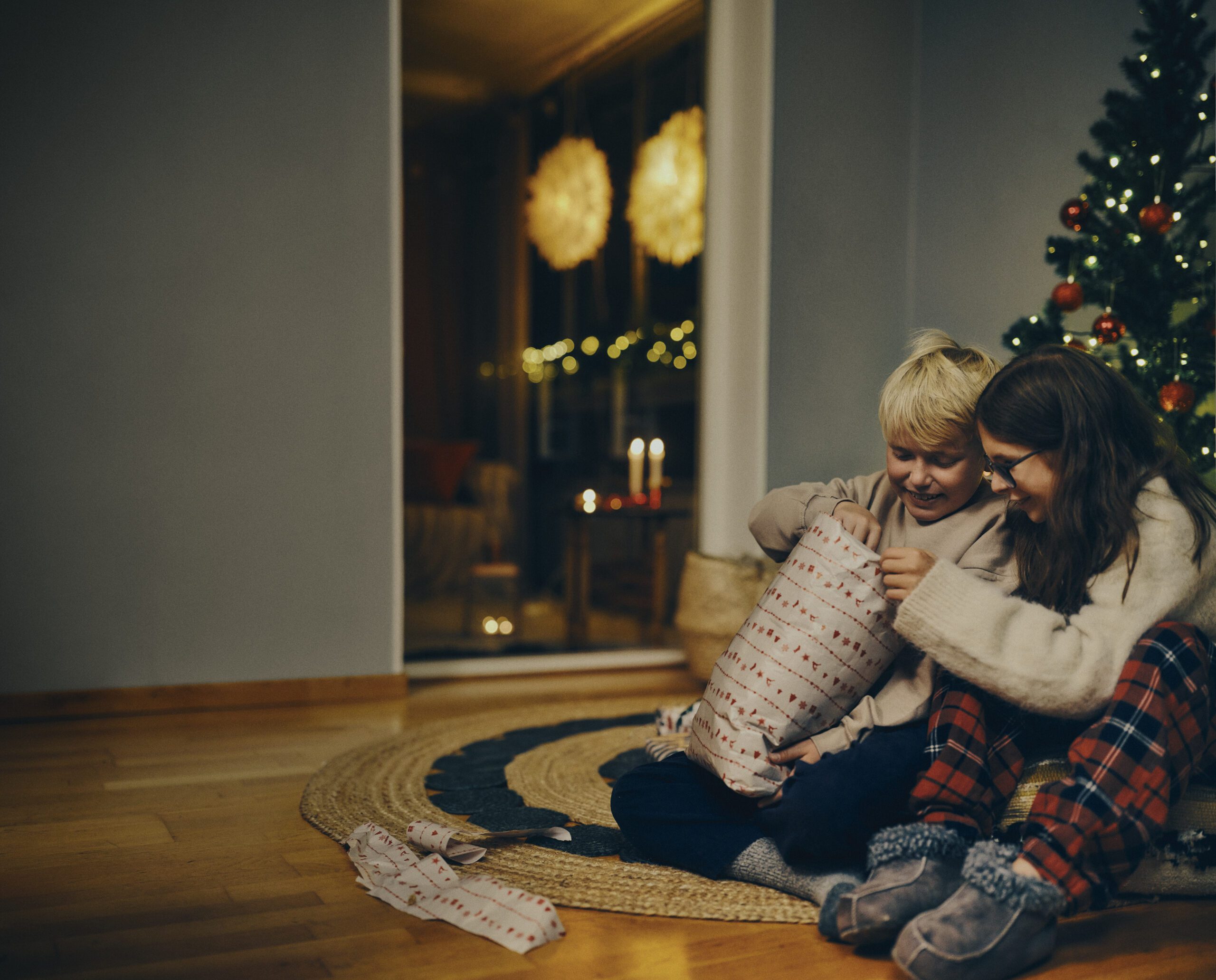 Bror, 11 år, sitter vid granen med en inslagen julklapp i famnen.